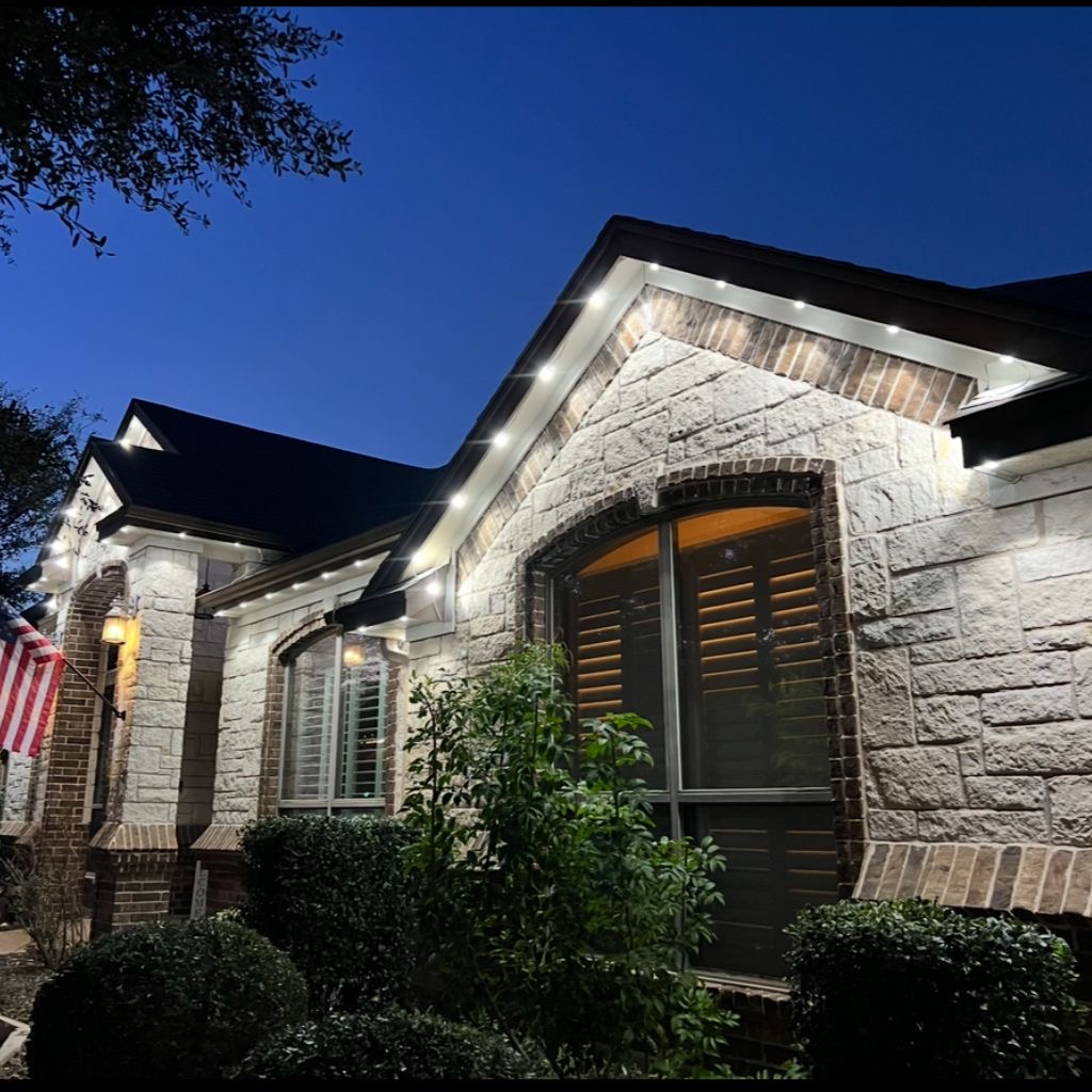 Stone home with warm white permanent lighting installed beneath the eaves